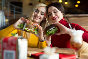 Two happy girls bite burgers. Concept of fast food